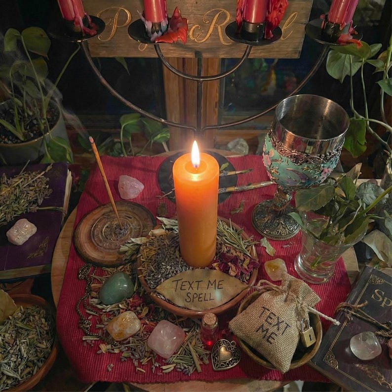 Puede incluir: Una vela encendida sobre una mesa con varios objetos, incluyendo cristales, hierbas, un c&aacute;liz y una peque&ntilde;a bolsa con el texto "TEXT ME". Un letrero de madera con las letras "P" y "R" es visible en el fondo. Tema m&iacute;stico.