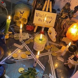 May include: A ritual altar setup featuring a pentagram mat, a skull with a symbol, a small sign reading WitchFwen On Etsy, a Hecate's Protection candle, gold coins, paper money, a green drawstring pouch, a ritual dagger, and several lit candles.