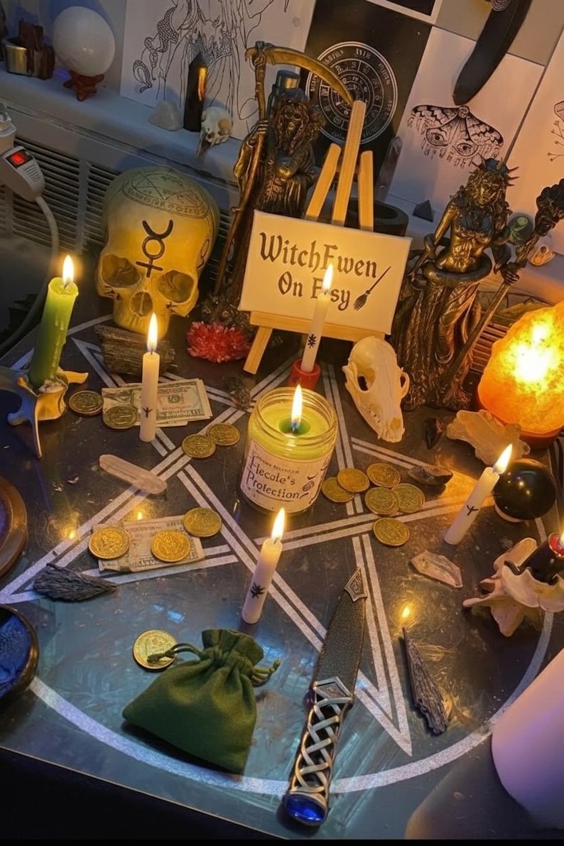 May include: A ritual altar setup featuring a pentagram mat, a skull with a symbol, a small sign reading WitchFwen On Etsy, a Hecate's Protection candle, gold coins, paper money, a green drawstring pouch, a ritual dagger, and several lit candles.