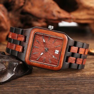 Puede incluir: Reloj de pulsera de madera con esfera cuadrada y correa de madera marr&oacute;n. La esfera es de color marr&oacute;n rojizo con agujas e indicadores plateados. La fecha se muestra a las 3 en punto. La correa est&aacute; hecha de segmentos de madera claros y oscuros alternados.
