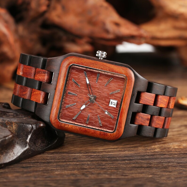 Puede incluir: Reloj de pulsera de madera con esfera cuadrada y correa de madera marr&oacute;n. La esfera es de color marr&oacute;n rojizo con agujas e indicadores plateados. La fecha se muestra a las 3 en punto. La correa est&aacute; hecha de segmentos de madera claros y oscuros alternados.