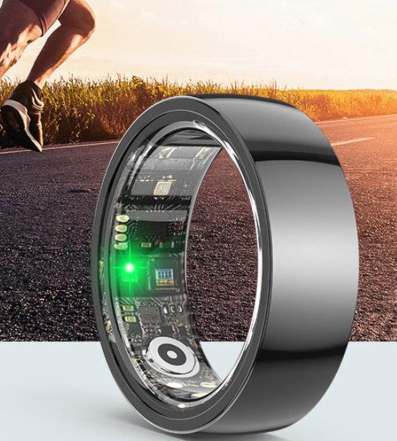 May include: A black smart ring with a clear inner band displaying circuit board components and a green light. The ring is shown with a runner in the background, suggesting fitness tracking capabilities. The ring has a sleek, modern design.