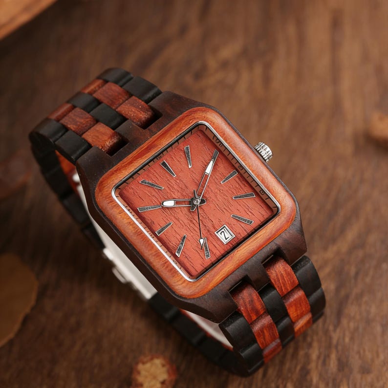 Puede incluir: Un reloj de pulsera de madera con esfera cuadrada y correa marr&oacute;n y negra. La esfera es de color marr&oacute;n rojizo con agujas e indicadores plateados. La fecha se muestra a las 3 en punto. El reloj es de madera.