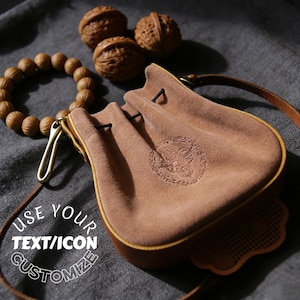 Può includere: Un sacchetto in camoscio marrone con coulisse e design in rilievo, un braccialetto di perline di legno e tre noci. Il sacchetto ha un cinturino in pelle e una chiusura color oro. È visibile anche il testo "USE YOUR TEXT/ICON CUSTOMIZE".