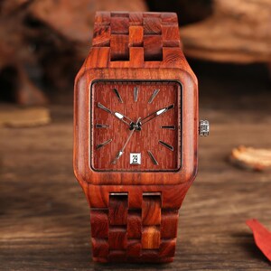 Puede incluir: Un reloj de pulsera de madera con una esfera cuadrada y una correa a juego. La esfera del reloj es de color marr&oacute;n rojizo con manecillas e indicadores plateados. La fecha se muestra como el n&uacute;mero 29. El reloj est&aacute; hecho de madera marr&oacute;n rojiza.