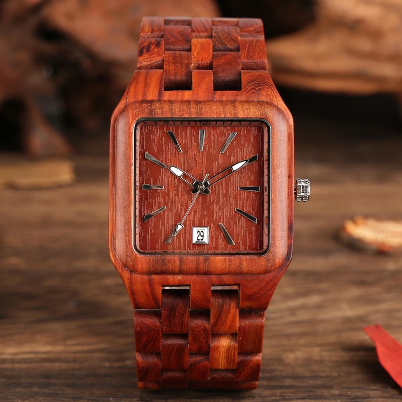 Puede incluir: Un reloj de pulsera de madera con una esfera cuadrada y una correa a juego. La esfera del reloj es de color marr&oacute;n rojizo con manecillas e indicadores plateados. La fecha se muestra como el n&uacute;mero 29. El reloj est&aacute; hecho de madera marr&oacute;n rojiza.