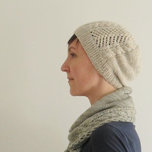 Puede incluir: Una persona lleva un gorro de punto beige claro con un patr&oacute;n de encaje y una bufanda de punto beige claro a juego. La bufanda est&aacute; drapeada alrededor del cuello y los hombros de la persona.
