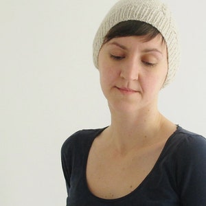 Puede incluir: Una mujer con una boina de punto beige claro con un dise&ntilde;o sencillo. Lleva una camiseta azul oscuro de cuello redondo.