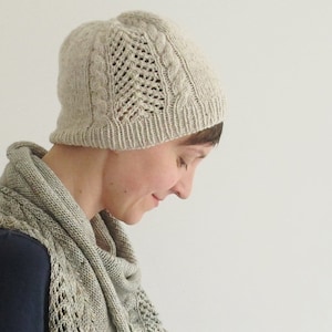 Puede incluir: Una mujer lleva un gorro de punto beige claro con un patr&oacute;n de trenzas y una bufanda a juego. El gorro tiene un delicado dise&ntilde;o de encaje.