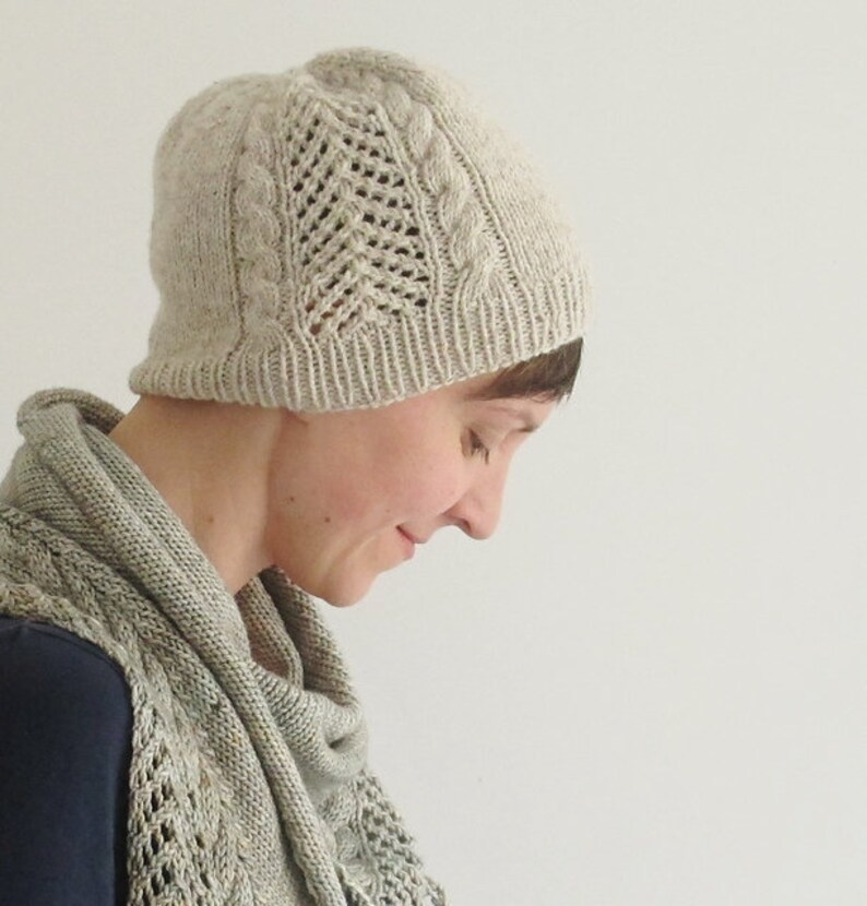 Puede incluir: Una mujer lleva un gorro de punto beige claro con un patr&oacute;n de trenzas y una bufanda a juego. El gorro tiene un delicado dise&ntilde;o de encaje.