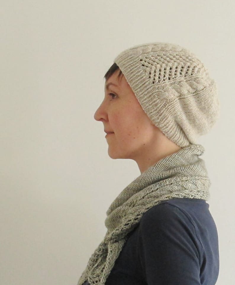 Puede incluir: Una persona lleva un gorro de punto beige claro con un patr&oacute;n de encaje y una bufanda de punto beige claro a juego. La bufanda est&aacute; drapeada alrededor del cuello y los hombros de la persona.