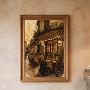 May include: A framed wall art print depicting a sepia-toned street scene of an outdoor cafe at dusk with string lights, patrons seated at tables, and a chalkboard sign, displayed on a textured beige wall above a small round bistro table.