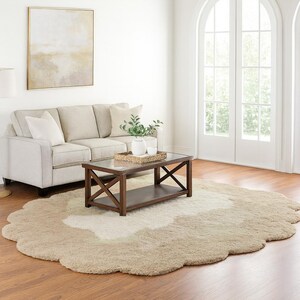 May include: A living room scene featuring a beige sofa, a dark brown coffee table with a glass top, and a large, uniquely shaped rug in shades of beige and cream. A framed artwork hangs on the wall, and a white door is visible.