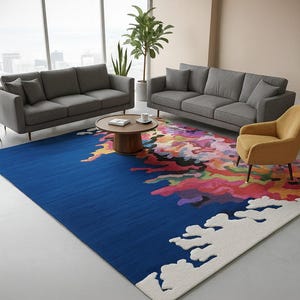 May include: A modern living room setup featuring a large blue area rug with a colorful abstract design. Two gray sofas, a yellow armchair, and a wooden coffee table complete the space. A tall plant and large windows are also visible.