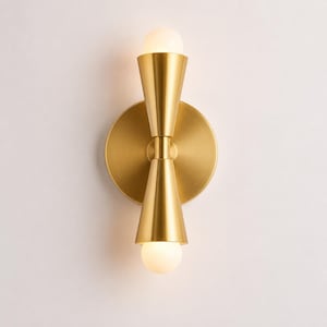 May include: A wall sconce featuring a circular brass backplate and two vertical, cone-shaped brass shades pointing in opposite directions. Each cone houses a small, spherical white light bulb at its tip, creating a symmetrical lighting fixture.