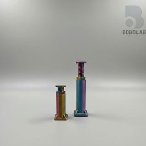 May include: Two iridescent metal jacks, one tall and one short, stand against a neutral background. The jacks have a square base, a cylindrical body, and a threaded top. The colors shift from purple to green and gold.