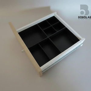 Peut inclure: Tiroir blanc ouvert avec façade en bois clair et compartiments intérieurs noirs. Le tiroir est divisé en plusieurs sections de tailles variables, parfait pour organiser de petits objets. Le logo "BOBOLAB" est visible dans le coin supérieur droit.