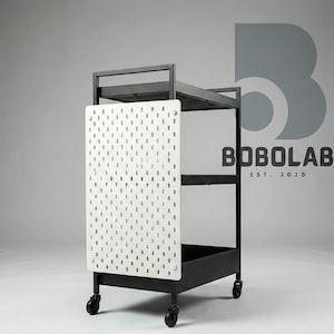 Könnte beinhalten: Schwarzer Metall-Servierwagen mit weißer Lochwandseite. Der Wagen hat drei Regale und eine untere Ablage, die alle von einem schwarzen Rahmen und Rollen getragen werden. Der Text "BOBOLAB EST. 2025" ist im Hintergrund sichtbar.