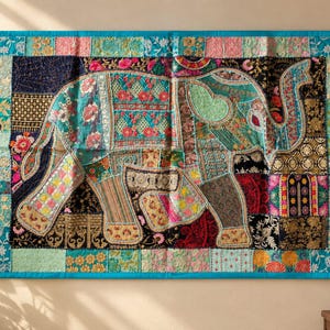 Pode incluir: Uma tapeçaria retangular com um design de patchwork e um motivo central de elefante. O tecido apresenta vários quadrados de tecido em tons de turquesa, rosa, dourado e preto, decorados com padrões florais intrincados e bordados detalhados.