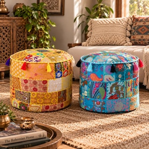 May include: Two round floor poufs featuring patchwork fabric designs. The left pouf is primarily yellow and orange with floral patterns and colorful tassels. The right pouf is primarily blue and turquoise with paisley and floral prints and tassels.