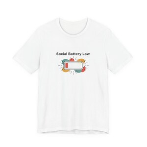Könnte beinhalten: Weißes T-Shirt mit dem Text "Social Battery Low" und einer Grafik einer leeren Batterie. Die Grafik zeigt ein Rechteck mit rotem Balken, umgeben von bunten Formen.