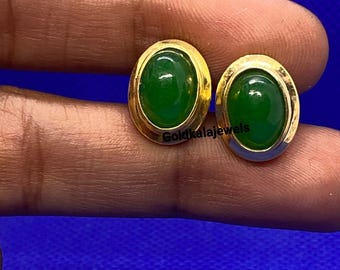 Könnte beinhalten: Ein Paar goldfarbene ovale Ohrstecker mit leuchtend grünen Edelsteinen. Die Ohrringe sind in einer goldenen Lünette gefasst und vor blauem Hintergrund präsentiert. Der Text "Goldkalajewels" ist sichtbar.