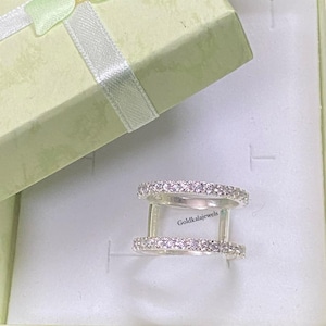 May include: A double-band silver ring featuring two parallel rows of small, clear, sparkling stones. The ring is stamped with 925 and the text Goldkalajewels. It is presented inside a light green gift box with a matching ribbon on the lid.