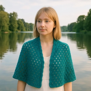 Op de afbeelding: Een turquoise gehaakte sjaal met een open weefpatroon. De sjaal is over de schouders gedrapeerd en toont een gestructureerd patroon. De turquoise kleur is levendig en het open weefsel geeft een delicate, luchtige uitstraling. De sjaal wordt over een wit kledingstuk gedragen.