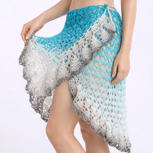 May include: A crochet skirt in shades of blue and white, with a ruffled edge. The skirt has a wrap design and is made of a lightweight, open-weave material. The skirt is a beach cover-up.