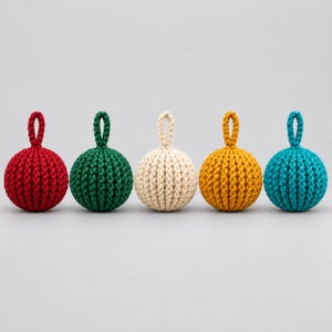 May include: Five spherical ornaments arranged in a row, each featuring a textured, braided knit pattern and a small matching loop at the top. The colors from left to right are deep red, forest green, cream, mustard yellow, and bright teal.