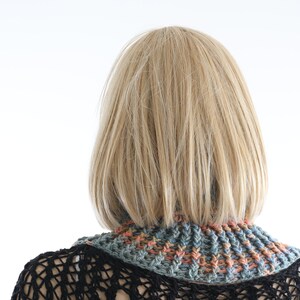 May include: A woman with blonde hair is wearing a crocheted neck warmer with a multi-colored pattern of blue, green, and orange. The neck warmer is made of a soft, chunky yarn.