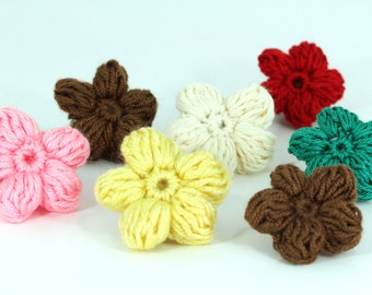 May include: Seven crocheted flower embellishments in various colors, including pink, brown, white, yellow, green, and red. The flowers are all the same size and shape, with five petals and a small center.