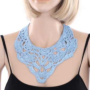 May include: A light blue crocheted collar necklace. The necklace is made of delicate, intricate stitches and has a scalloped edge.