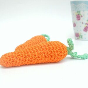 May include: Two crocheted carrots with green tops. The carrots are orange and the tops are a light green.