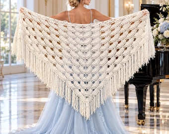May include: A cream-colored triangular crochet shawl featuring an intricate repeating fan pattern and long fringe along the bottom edges. The shawl is crafted with a delicate openwork design and is displayed spread out to show the full texture.