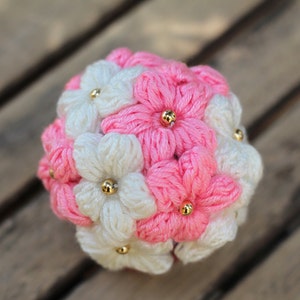 May include: A crocheted flower bouquet made of pink and white yarn with gold beads in the centre of each flower.