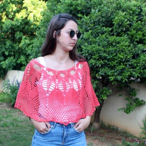 Puede incluir: Un top de crochet de color coral con un delicado diseño calado. El top es corto y tiene un corte holgado.