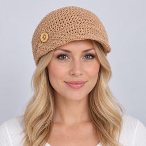 May include: A tan crocheted newsboy cap featuring a textured, open-weave pattern and a short, stiff brim. A single, round, light-colored wooden button is attached to the side of the cap, providing a decorative accent to the structured design.