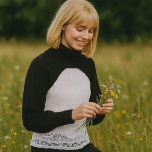 Pode incluir: Um bolero de malha preta com gola alta e mangas compridas usado sobre uma blusa branca sem mangas com uma delicada sobreposição de renda com padrão floral e bainha recortada. A combinação das peças cria um visual em camadas.