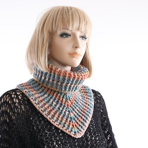May include: A crocheted cowl with a geometric pattern in shades of blue, pink, and brown. The cowl is worn by a mannequin with blonde hair.