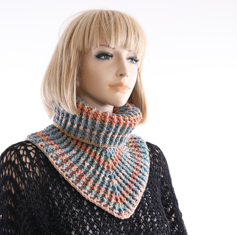 May include: A crocheted cowl with a geometric pattern in shades of blue, pink, and brown. The cowl is worn by a mannequin with blonde hair.