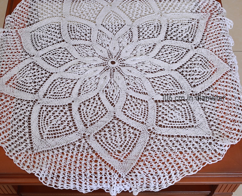 May include: A white, intricately crocheted doily with a floral design. The doily measures 106 cm in diameter. The delicate openwork pattern creates a lace-like effect, perfect for adding a touch of elegance to any space.