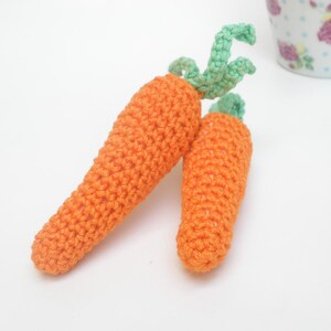 May include: Two crocheted carrots with green tops. The carrots are orange and the tops are a light green.