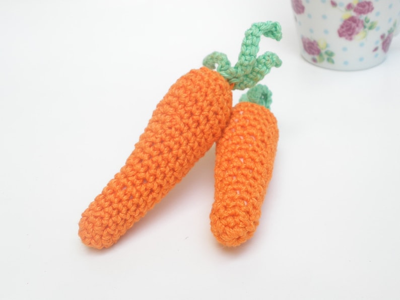 May include: Two crocheted carrots with green tops. The carrots are orange and the tops are a light green.