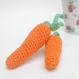 May include: Two crocheted carrots with green tops. The carrots are orange and the tops are a light green.
