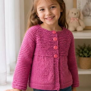 May include: A bright magenta long-sleeved knit cardigan featuring a round neckline and four matching circular buttons down the front. The garment is constructed with a textured garter stitch pattern on the yoke and sleeves, transitioning to a smooth stockinette stitch on the lower body.