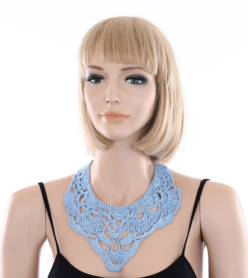 May include: A light blue crocheted collar necklace with a delicate floral pattern.