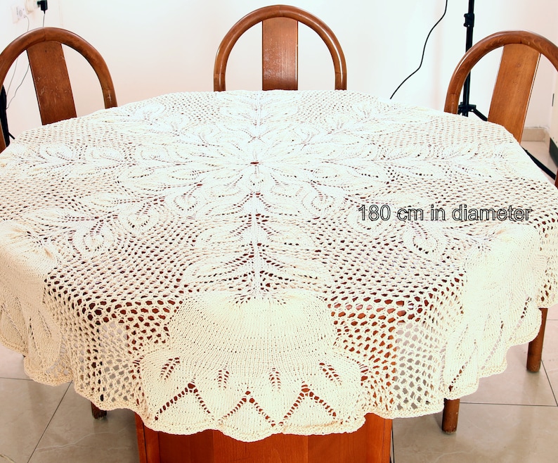 Puede incluir: Un mantel de crochet blanco con un delicado patr&oacute;n floral. El mantel tiene 180 cm de di&aacute;metro y est&aacute; colocado sobre una mesa de madera.