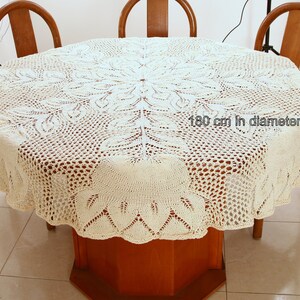Puede incluir: Un mantel de crochet blanco con un delicado patr&oacute;n floral. El mantel tiene 180 cm de di&aacute;metro y est&aacute; puesto sobre una mesa de madera.