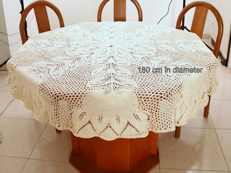 Puede incluir: Un mantel de crochet blanco con un delicado patr&oacute;n floral. El mantel tiene 180 cm de di&aacute;metro y est&aacute; puesto sobre una mesa de madera.